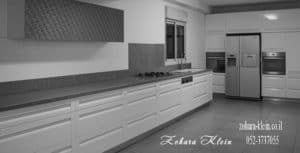 מטבח לבן מודרני כאשר ידיות הארונות אינטגראליות, הקו האחיד נותן טאץ למטבח המשולב בו קלאפה ארוכה לאחסון עילי