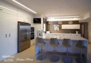 מטבח מודרני – ארונות המטבח עשוי זכוכית עם ידיות אינטגראליות תואמות לחיפוי המטבח וגם דלת נסתרת לחדר העבודה